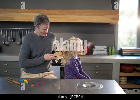 Padre figlie di spazzolatura capelli permanente, mentre in cucina Foto Stock