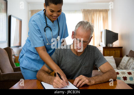 Medico donna assistere uomo senior per iscritto presso la casa di cura Foto Stock