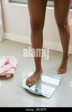 Sezione bassa della donna in piedi sulla bilancia in bagno a casa Foto Stock