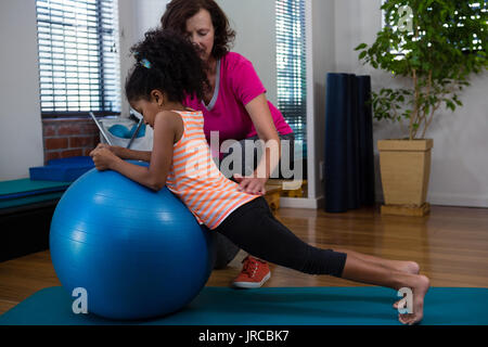 Fisioterapista femminile aiutando ragazza paziente di eseguire esercizi di allungamento sul tappeto di esercizio in clinica Foto Stock