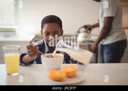 Ragazzo versando il latte in cereali per la prima colazione la ciotola in cucina a casa Foto Stock