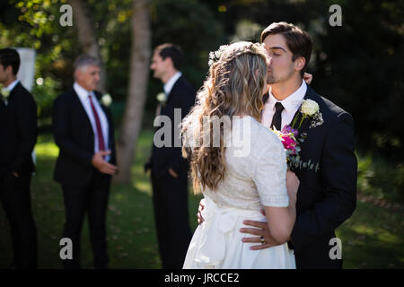 Affettuosa groom kissing sposa sulla fronte in posizione di parcheggio Foto Stock