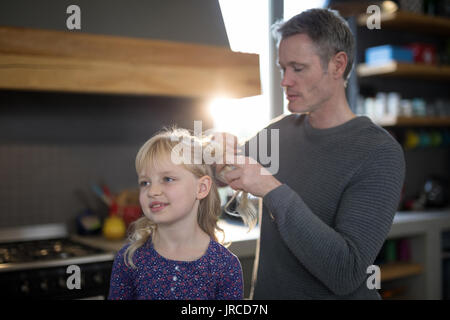 Padre figlie fissante per capelli permanente, mentre in cucina Foto Stock