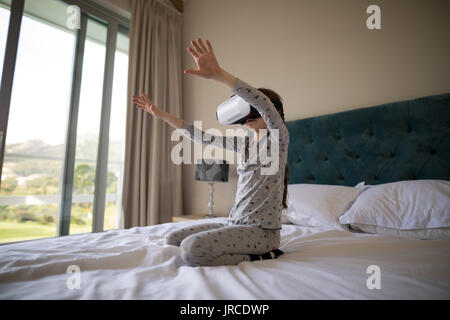 Ragazza con la realtà virtuale auricolare sul letto in camera da letto Foto Stock