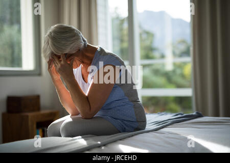 Tense senior donna seduta sul letto in camera da letto a casa Foto Stock