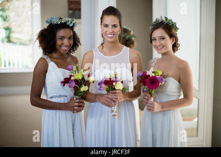 Ritratto di sposa e le sue damigelle hanno piedi con bouquet a casa Foto Stock