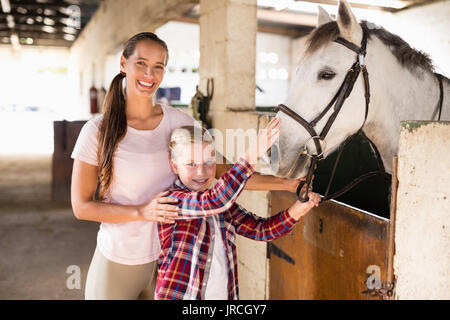 Ritratto di sorelle stroking cavallo mentre sta in piedi in modo stabile Foto Stock