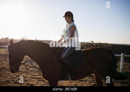 Vista laterale del fantino femmina di equitazione al granaio Foto Stock