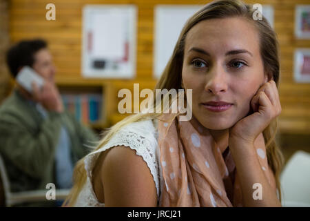 Premurosa donna che guarda lontano mentre l uomo che parla al telefono in background al cafe Foto Stock