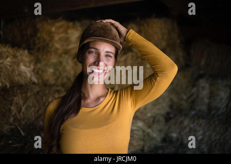 Ritratto di felice jockey femmina in piedi contro il fieno in stabile Foto Stock