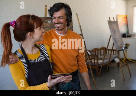 Amici sorridente guardando ogni altro tenendo tavoletta digitale in classe d'arte Foto Stock