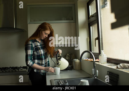 Giovane donna versando il tè nel bicchiere mentre in piedi in cucina Foto Stock