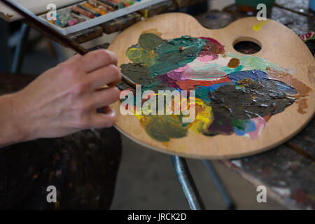 Ritagliate la mano sulla persona che tiene il pennello sulla tavolozza dei colori Foto Stock