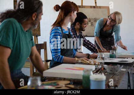 Maestro sorridente esaminando la pittura mentre in piedi da studente in classe d'arte Foto Stock