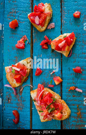 Bruschetta con pane toscano con pomodori e cipolle su un arrugginito blu sullo sfondo di legno, vista dall'alto. Alta risoluzione i dettagli. Foto Stock