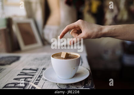 Una donna messa cubetto di zucchero in сup di caffè nella caffetteria Foto Stock