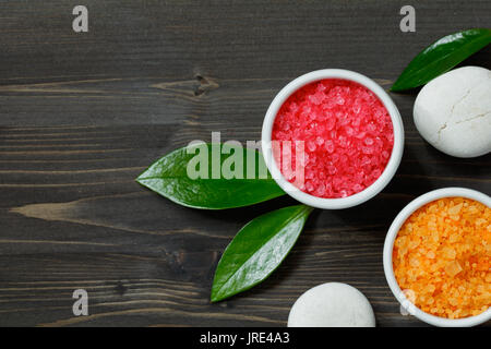 Vista dall'alto di un cosmetico rosa e arancio sale di mare su tavoli in legno nero. Foto Stock