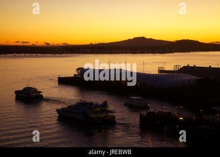 Sunset over Rangitoto Island, Waitemata Harbour, 'Cloud' edificio eventi su Queens Wharf e traghetti passeggeri, Auckland, North Island, New Zeala Foto Stock