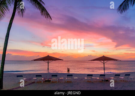 Un paio di passeggiare sulla Seven Mile Beach nei Caraibi al tramonto, Grand Cayman, Isole Cayman Foto Stock