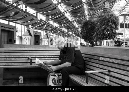 Uomo che legge il giornale seduto su un banco a Göteborg la stazione centrale degli autobus. Foto Stock