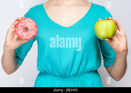 Bella giovane donna in abito verde azienda apple e ciambella. studio shot su sfondo grigio chiaro Foto Stock