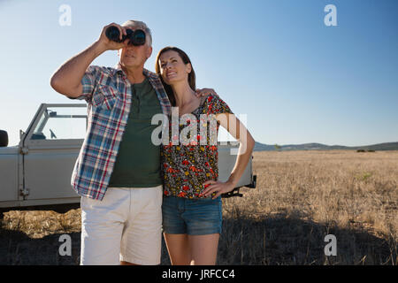 L'uomo con la donna guardando attraverso il binocolo dal veicolo parcheggiato sul paesaggio Foto Stock