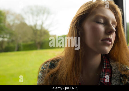 Close up di donna con gli occhi chiusi appoggiato sulla finestra mentre è seduto Foto Stock