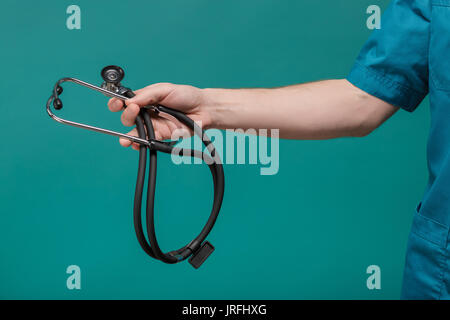 Medico maschio tenendo il suo stetoscopio in mano sullo sfondo blu Foto Stock
