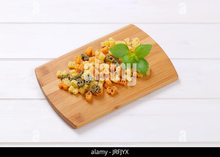 Pila di greggio di pasta colorata sul tagliere di legno Foto Stock