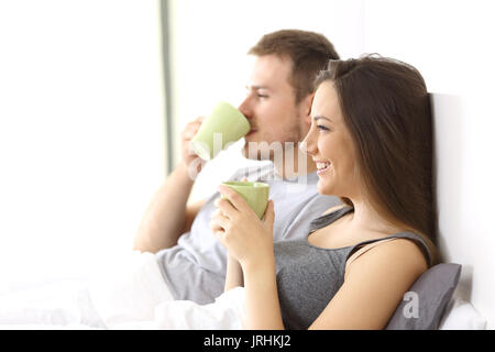 Vista laterale di una rilassata atmosfera giovane avente colazione tazze di contenimento sul letto di una camera di albergo o casa Foto Stock