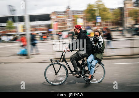 Amsterdam, Paesi Bassi - 27 April, 2017: un uomo ciclista trasporta una giovane donna come passeggero su una bicicletta, Equitazione attraverso le strade di Amsterdam, Nether Foto Stock