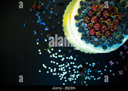 Festosa torta decorata con ciliegie fresche e fiori scuri su un tavolo di legno Foto Stock