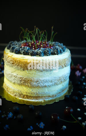 Festosa torta decorata con ciliegie fresche e fiori scuri su un tavolo di legno Foto Stock