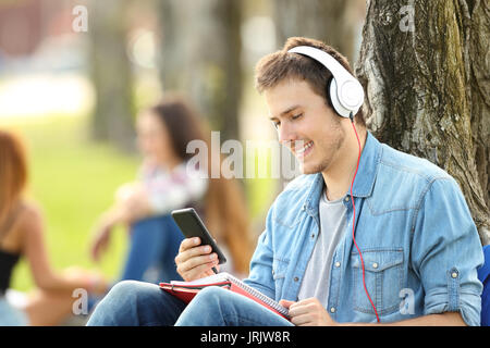 L apprendimento degli studenti in ascolto tutorials audio in un parco seduta sul prato di un parco Foto Stock