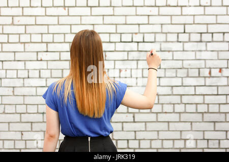 Il concetto di apprendimento. La ragazza è al bianco muro di mattoni. Foto per il tuo design. Contiene una penna nelle sue mani. Sta con la sua schiena. Istruzione moderna online. Foto Stock