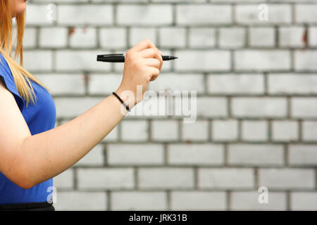 Il concetto di apprendimento. La ragazza è al bianco muro di mattoni. Foto per il tuo design. Contiene una penna nelle sue mani. Sorge nel profilo. Istruzione moderna online. Ri Foto Stock