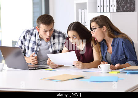 Tre dipendenti stupito la lettura di un documento cartaceo in ufficio Foto Stock