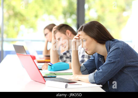 Vista laterale di tre studenti frustrato cercando di imparare on line in aula con uno sfondo verde Foto Stock