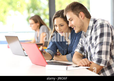 Due concentrati gli studenti che studiano in linea insieme seduti in un desktop in una classe con un compagno di classe in background Foto Stock