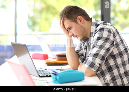 Vista laterale del singolo studente frustrato cercando di risolvere il difficile problema sulla linea seduto in una scrivania in aula Foto Stock