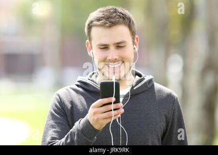 Vista frontale di un ragazzo adolescente ascoltare musica on line con auricolari e un telefono intelligente Foto Stock