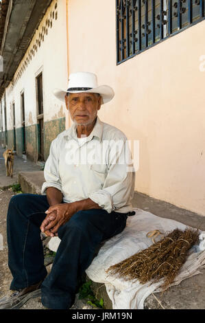 Uomo in cappello bianco si siede accanto a fasci di rami per addensarsi di fuochi in Honduras Foto Stock