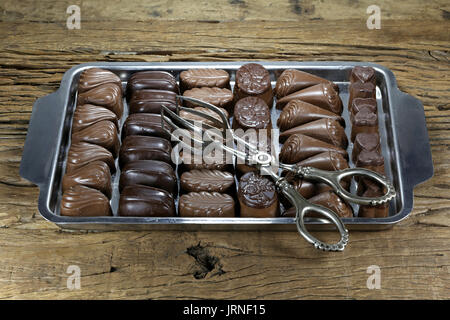 Vassoio con belga praline di cioccolato e pasticceria tong su rustico sfondo di legno Foto Stock