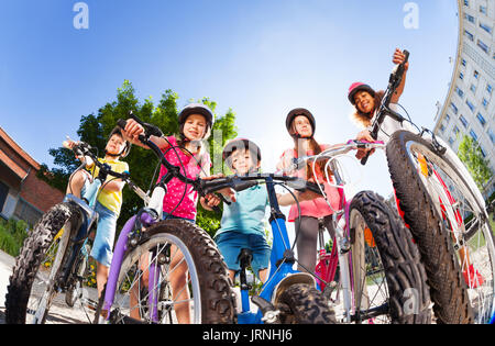 Angolo basso ritratto di cinque happy bike rider, due ragazzi e tre ragazze, in piedi in una linea contro il cielo blu Foto Stock