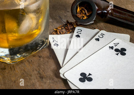 White carte da gioco, un tubo di fumo con fuoriuscita di tabacco e un bicchiere di whiskey con ghiaccio, sulla parte superiore di una tavola di legno Foto Stock