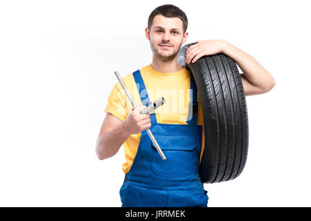 Lavoratore di servizio in uniforme blu detiene il pneumatico in mano, sfondo bianco, aggiustatore con pneumatico Foto Stock