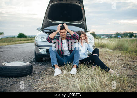 Stanco uomo e donna seduta contro rotture di auto con il cofano aperto. Problemi con veicolo su strada nel giorno di estate Foto Stock