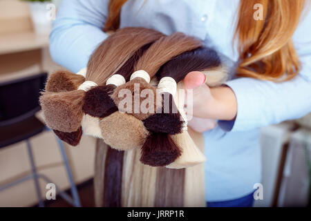 Donna capelli detiene attrezzature di estensione dei capelli naturali. i campioni di capelli di diversi colori Foto Stock