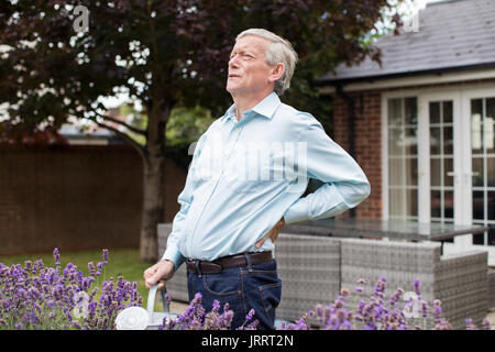 Uomo maturo che soffrono di mal di schiena mentre il giardinaggio a casa Foto Stock