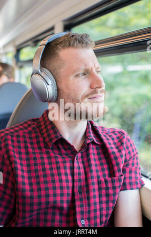 Giovane uomo che ascolta la musica in cuffia durante il viaggio di lavoro Foto Stock